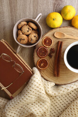 Cup of tea or coffee, various spices, bowl of cookies, tangerines, books, reading glasses and knitted blanket on wooden table. Hygge at home concept, flat lay.