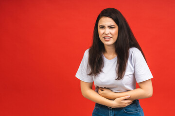 Young beautiful woman having abdominal pain isolated on red background.