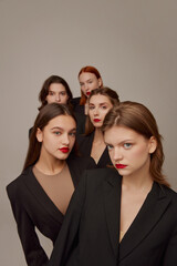 Portrait of young beautiful women in black jackets and red lipstick makeup posing over grey background. Models look