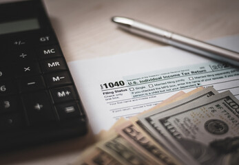 U.S. individual income tax return on a wooden table next to a calculator, dollars, money, a pen and a notepad. Blank US tax forms. Retro old style photo. - 544391324