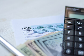 U.S. individual income tax return on a wooden table next to a calculator, dollars, money, a pen and a notepad. Blank US tax forms.