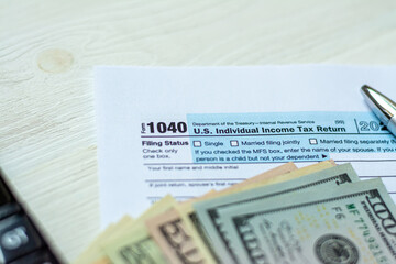U.S. individual income tax return on a wooden table next to a calculator, dollars, money, a pen and a notepad. Blank US tax forms.
