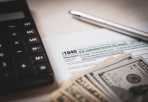 U.S. individual income tax return on a wooden table next to a calculator, dollars, money, a pen and a notepad. Blank US tax forms. Retro old style photo.