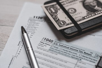 U.S. individual and corporation income tax return close-up next to a calculator, dollars, money, a pen and a notepad on a wooden table. Retro old style photo. - 544391524