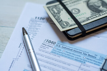 U.S. individual and corporation income tax return close-up next to a calculator, dollars, money, a pen and a notepad on a wooden table. - 544391552