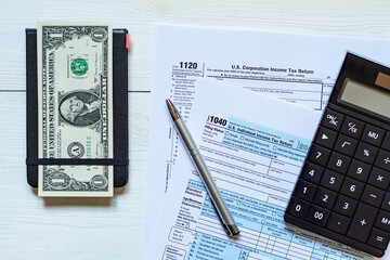 U.S. individual and corporation income tax return on a wooden table next to a calculator, dollars, money, a pen and a notepad. View from above.