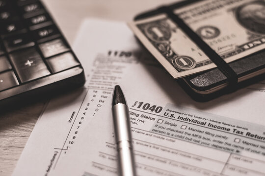 U.S. individual and corporation income tax return close-up next to a calculator, dollars, money, a pen and a notepad on a wooden table. Retro old style photo.