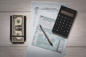U.S. individual and corporation income tax return on a wooden table next to a calculator, dollars, money, a pen and a notepad. View from above. Retro old style.
