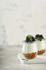Yogurt with granola, blackberry berry fruits and muesli served in glass jar on gray concrete table background. Healthy breakfast concept. Healthy food for breakfast, top view