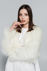 portrait of pretty young woman in stylish white faux fur jacket looking at camera isolated on grey.
