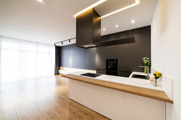 Large, empty room with black kitchen and wood floors