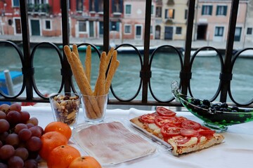 A magical view from the balcony of a house near the Venice canal. Italian pizza, prosciutto, olives and fruit for tonight. The olives are in a gondola made of glass on the island of Murano. 