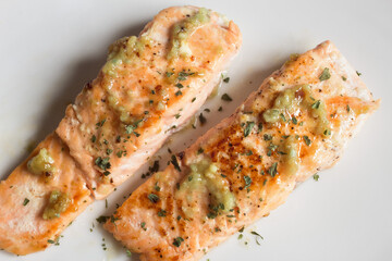 Overhead view of two lemon salmon loins with garlic and spices on a white plate. Fish and healthy food.