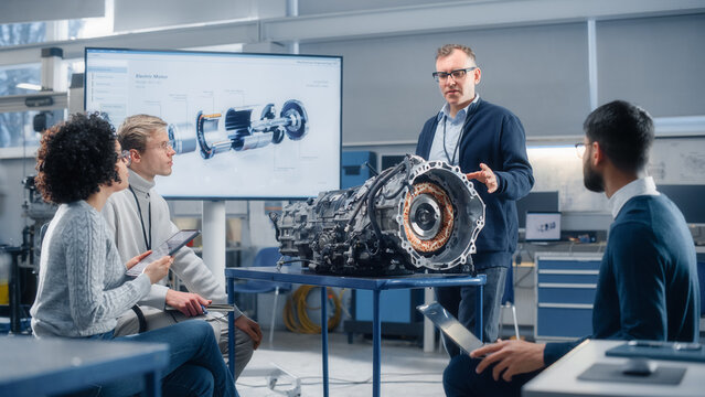 Team of Diverse Engineers Using Laptop and Tablet to Analyse Electric Vehicle Engine In the Research Laboratory. Modern Industry 4 Sustainable Energy and Emission Reduction Technology.
