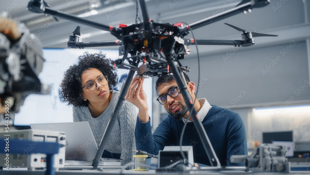 Poster Skilful Male Engineer with Semiconductor Gives Advice to Black Female Computer Developer While She is Writing Code for Drone Control. Technological and Innovative Startup Concept.