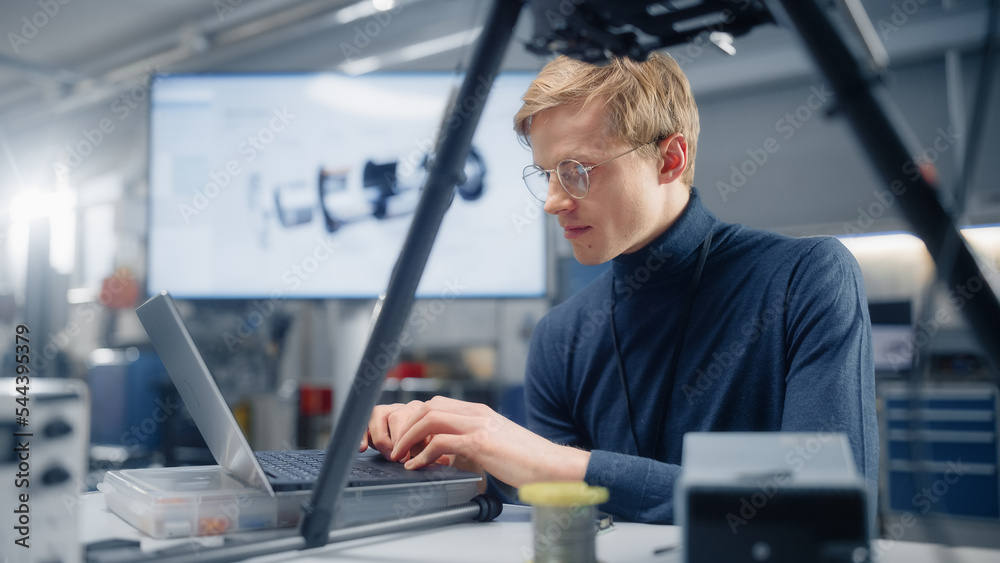 Poster young caucasian male engineer installs processor in the drone and types on laptop. designing unmanne