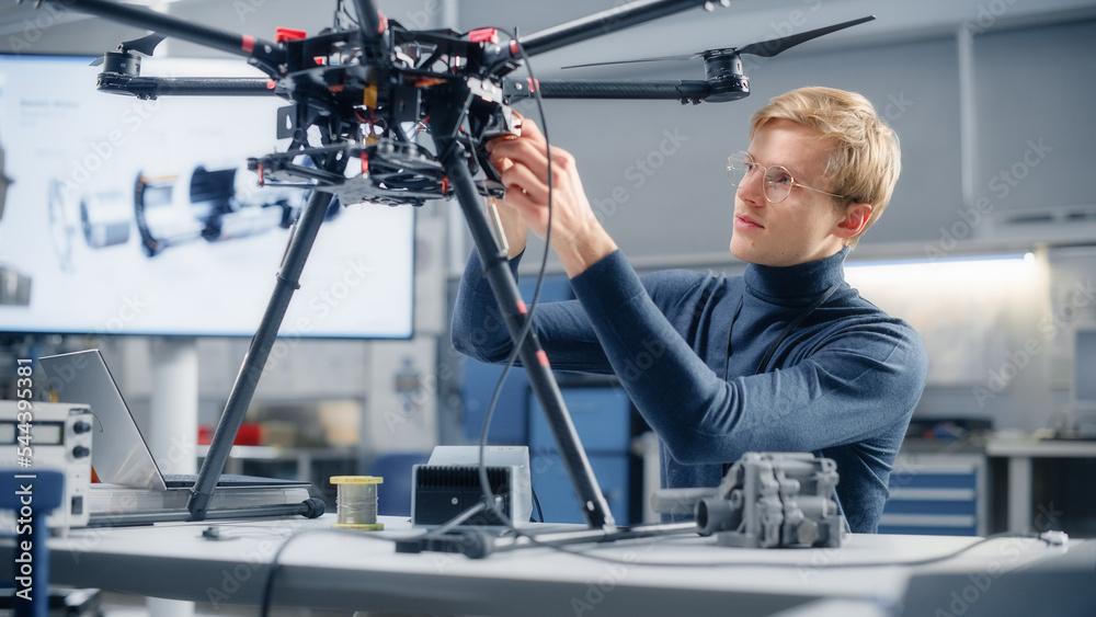 Poster young caucasian male engineer installs processor in the drone and types on laptop. designing unmanne