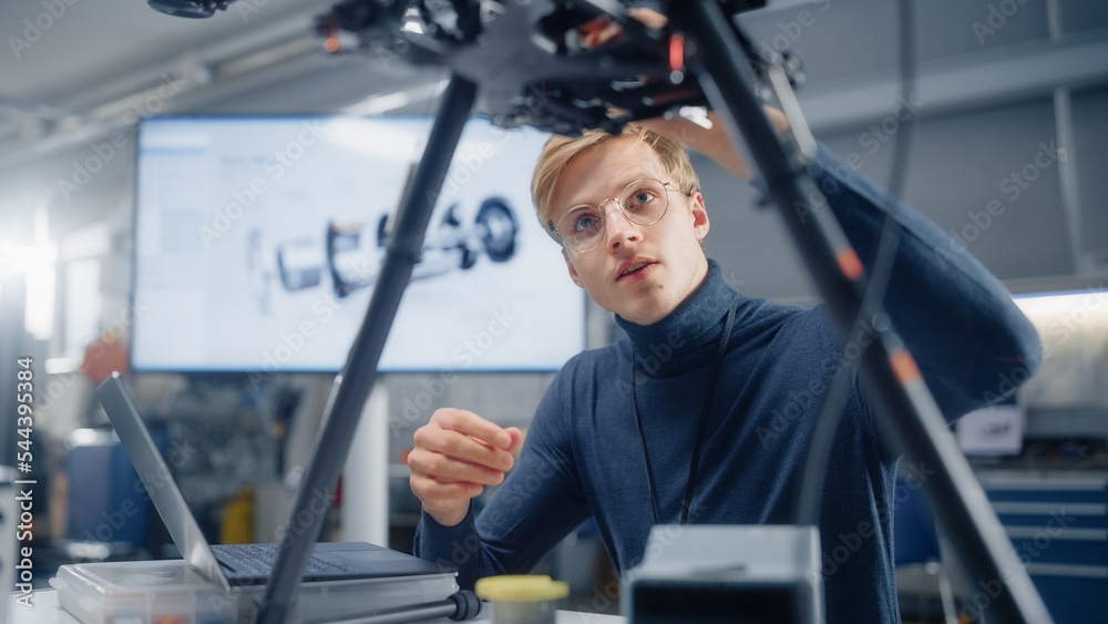 Poster young caucasian male engineer installs processor in the drone and types on laptop. designing unmanne