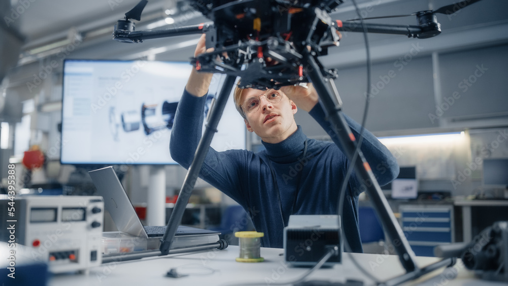 Poster young caucasian male engineer installs powerful processor in the drone and types on laptop. designin