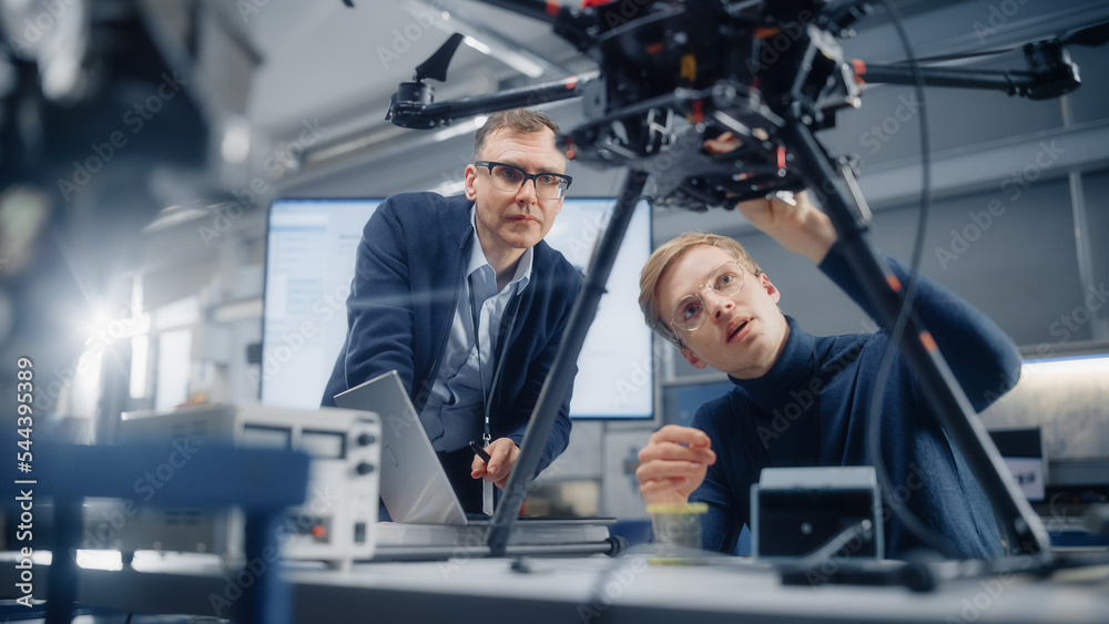 Poster Chief Engineer Looks at the Drone Attentively While Discussing Design with Promising Computer Scientist. Manufacturing Facility that Creates Modern Unmanned Aerial Vehicles.