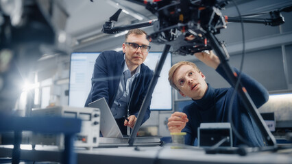 Chief Engineer Looks at the Drone Attentively While Discussing Design with Promising Computer Scientist. Manufacturing Facility that Creates Modern Unmanned Aerial Vehicles.