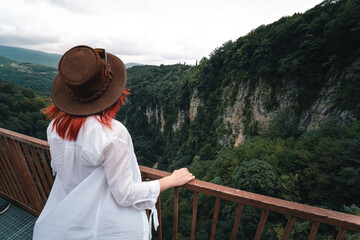 Fototapeta na wymiar Woman traveler in Okatse Canyon in Georgia, standing on hanging metal pedestrian pathway trail above deep precipice. Leather hat. Travel and vacation. Back view. copy space