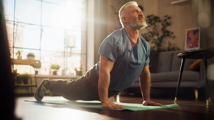 Strong Athletic Fit Senior Man Training on a Yoga Mat, Doing Back Stretching and Core Strengthening Exercises During Morning Workout at Home in Sunny Apartment. Concept of Health and Fitness.