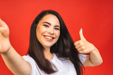 Portrait of pretty young happy woman making selfie on smartphone, isolated over red background.