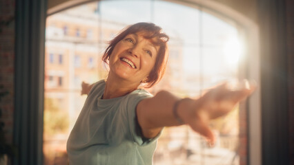Portrait of a Fit Middle Aged Woman with a Smile Stretching and Doing Core Strengthening Yoga Exercises During Morning Workout at Home in Bright Apartment. Health and Fitness Concept.