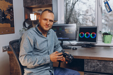 Smiling professional video editor with photo camera working in home studio with desktop computer...