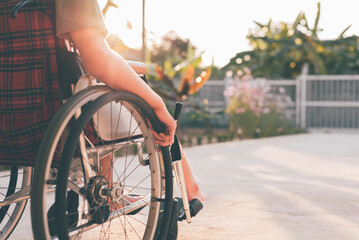 Naklejka premium Hand of young man with disability move wheelchair by himself in the ramp in garden of home or hospital,school,nursery with sunlight at sunset Positive photography and Good mental health concept.
