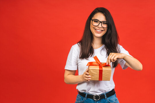 Happy holiday! Studio portrait of smiling young beautiful brunette woman holds gift box. Isolated over red background.