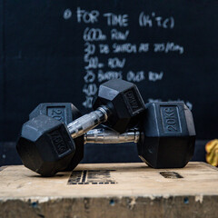 Closeup of two dumbbells on a wooden box in front of blackboard at the gym. Wod - workout of the day.