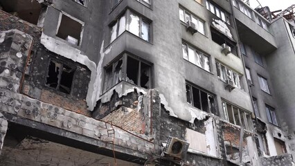 Exterior wall of bombed destroyed residential building with broken windows in Kyiv Ukraine. Ruined house outdoors on overcast cloudy day. Slow motion