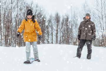 Fototapeta na wymiar Dad teaches his daughter to ride a snow skate in a winter park, family walk in the fresh air