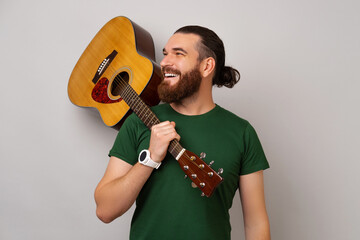 Strong handsome man wearing green T shirt is holding an acoustic guitar.