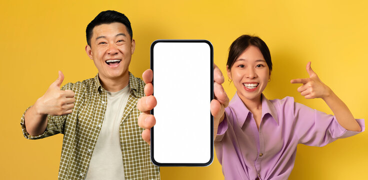 Smiling Asian Man And Woman Demonstrating Empty Smartphone With Big White Screen