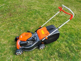 Motorized petrol garden lawnmower, orange-black color, standing on the lawn, view from the left