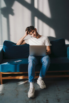 Portrait of an attractive man with cream on his cheeks, sitting on the couch in the living room, using laptop computer. Concept of young business people working