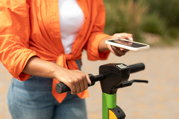 Young black female with smartphone pays money for ride on electric scooter in city park, close up, cropped