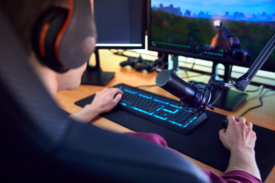 Close Up Of Man Gaming At Home Wearing Wireless Headphones Sitting At Desk With Multiple Monitors