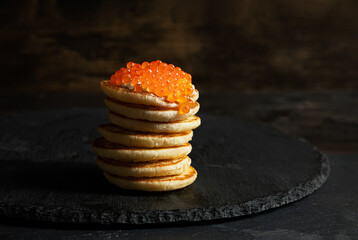 Red caviar on small pancakes blinis with sour cream on dark background