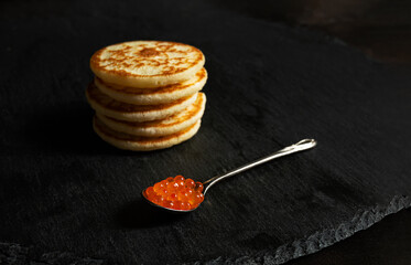 A spoonful of red caviar and small pancakes blinis on a slate