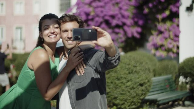 Happy young couple making selfie while spending time in park. Smiling Hispanic girl hugging her boyfriend taking photos from different angles with smartphone. Modern technology, romance concept.