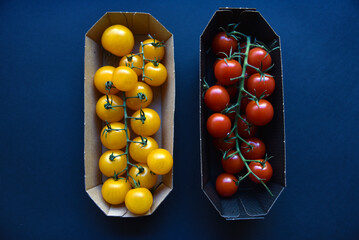 Small cherry tomatoes are yellow and red in a paper container. Small tomatoes on a black background.