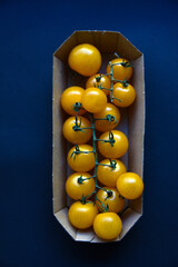 Small cherry tomatoes are yellow and red in a paper container. Small tomatoes on a black background.