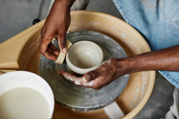 Top view of male hands of black young man using pottery wheel and creating handmade ceramics - obrazy, fototapety, plakaty