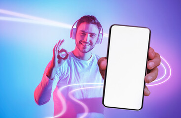 Handsome young man with headphones showing cell phone and okay