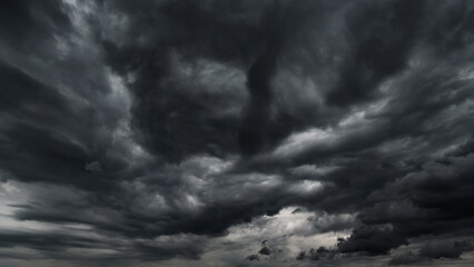 dark dramatic sky with black stormy clouds before rain or snow as abstract background, extreme weather, the sun shines through the clouds, high contrast photo