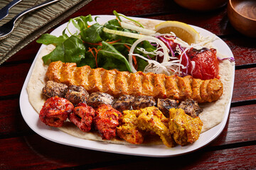 Chicken Mixed Grills platter with salad, lemon, bread served in dish isolated on table side view of middle east food